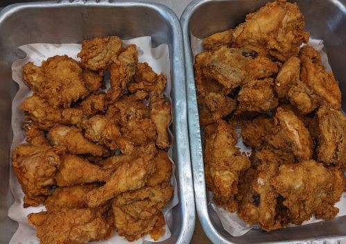 Two trays of crispy fried chicken pieces, golden brown and arranged on white paper.