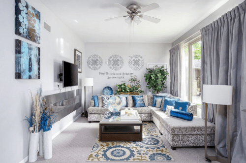 Bright living room with a patterned sofa, decorative pillows, a coffee table, and large windows letting in natural light.
