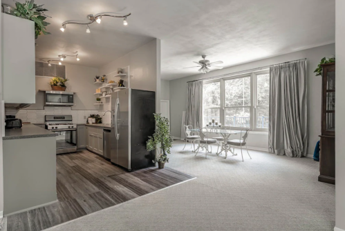 Bright, modern kitchen with stainless steel appliances, leading to a cozy dining area with a table and chairs by large windows.