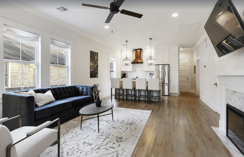 Modern living room with a blue sofa, round coffee table, and open kitchen featuring bar stools and stainless appliances.