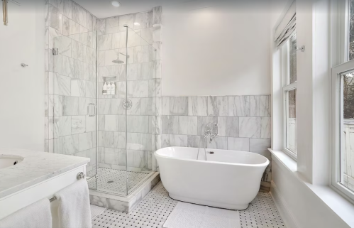 Modern bathroom featuring a glass shower, freestanding tub, and marble tile accents. Bright and airy with natural light.