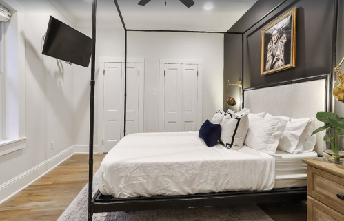 A modern bedroom featuring a four-poster bed, decorative pillows, a TV, and stylish wall art.