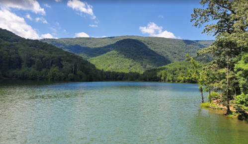A serene lake surrounded by lush green mountains under a clear blue sky.