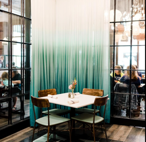 A cozy restaurant table with wooden chairs, surrounded by elegant curtains and a view of diners in the background.