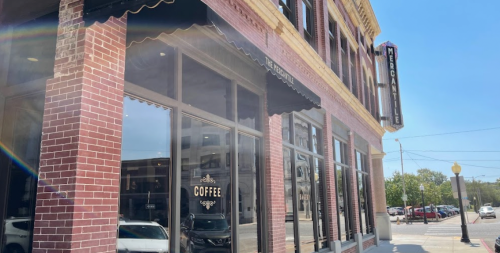 Exterior of a brick building with large windows, featuring a "Coffee" sign and a vintage marquee. Sunny day.