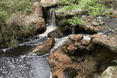 A serene landscape featuring a small waterfall cascading over rocky terrain into a dark, flowing stream.