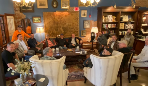 A group of men sitting in a cozy, well-decorated room, engaged in conversation around a coffee table.