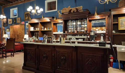 A vintage wooden bar with ornate details, mirrors, and glassware, set in a cozy, warmly lit room.