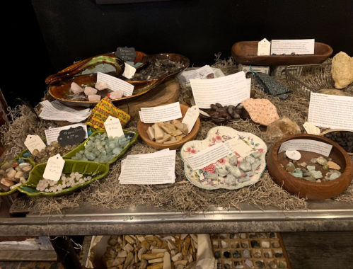 A display of various crystals and stones in bowls, with labels and descriptions on a table covered in moss.