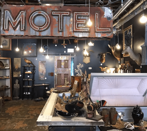Interior of a vintage motel-themed shop featuring eclectic decor, a coffin display, and various antique items.