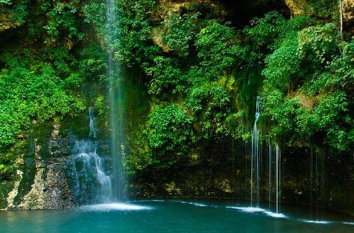 A serene waterfall cascading into a turquoise pool, surrounded by lush green foliage and rocky cliffs.