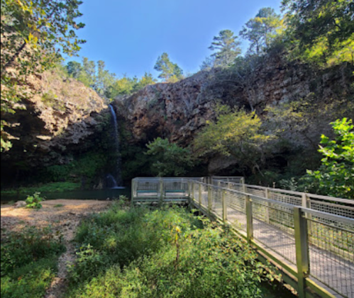 A serene waterfall cascades down rocky cliffs, surrounded by lush greenery and a wooden walkway.
