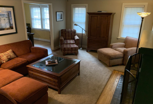 Cozy living room with two sofas, an armchair, a coffee table, and a wooden cabinet, featuring natural light from windows.