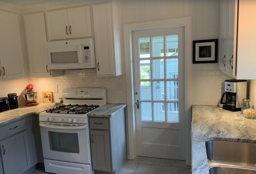 A modern kitchen featuring white cabinets, a gas stove, microwave, and a door leading outside. Marble countertops are visible.
