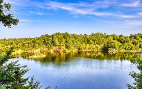 A serene lake surrounded by lush greenery under a clear blue sky, reflecting the landscape in calm waters.