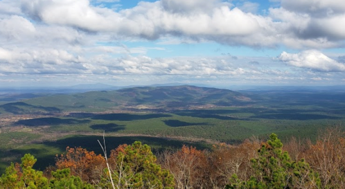 A panoramic view of rolling green hills and mountains under a partly cloudy sky.