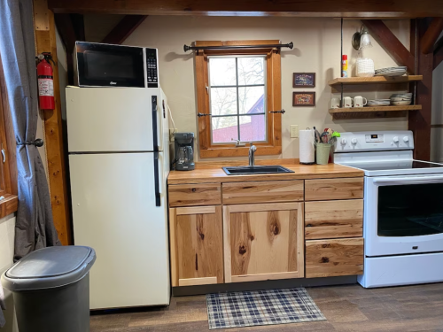 Cozy kitchen with wooden cabinets, white appliances, a sink, and a window overlooking a rustic view.