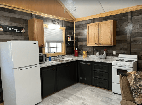 Cozy kitchen with wooden cabinets, a white fridge, stove, and rustic decor, featuring a chicken-themed centerpiece.