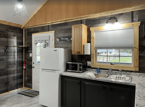 Cozy kitchen with a white fridge, microwave, and sink, featuring wooden accents and a window with a view.