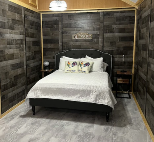 Cozy bedroom with a black bed, decorative pillows, wooden walls, and a sign reading "Blessed" above the bed.