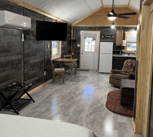 Cozy interior of a cabin with a kitchen, dining area, and seating, featuring wood accents and modern appliances.