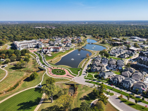 Aerial view of a residential area with ponds, green spaces, and well-maintained homes under a clear blue sky.