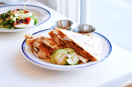 A plate of quesadillas with cucumber slices and two small bowls of dipping sauce.