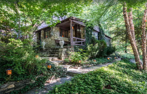 A charming stone cottage surrounded by lush greenery and lanterns, nestled in a serene forest setting.