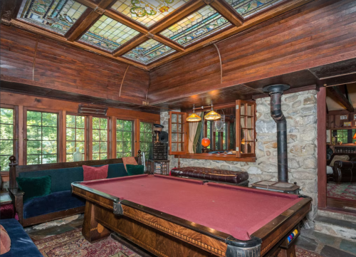 Cozy game room featuring a pool table, stained glass ceiling, wooden walls, and large windows with a view.