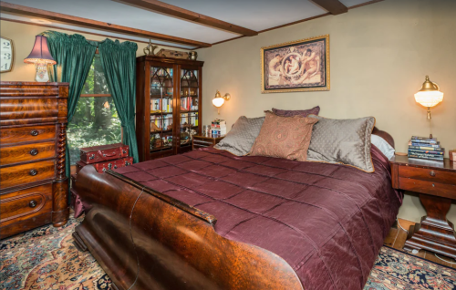 Cozy bedroom featuring a wooden sleigh bed, rich burgundy bedding, bookshelves, and warm lighting.