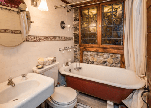 Cozy bathroom featuring a vintage tub, stone wall, and wooden accents, with a round mirror and decorative bowl.