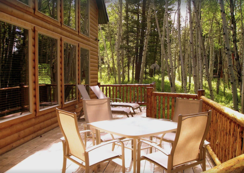 A wooden deck with a table and chairs, surrounded by trees and greenery in a serene outdoor setting.