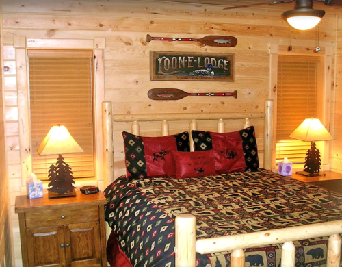 Cozy log cabin bedroom with a wooden bed, decorative pillows, lamps, and rustic decor on the walls.