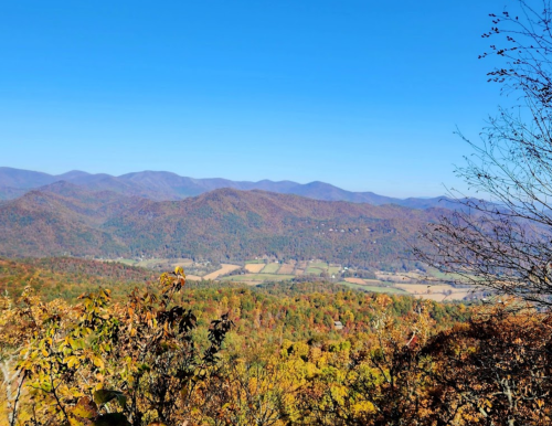 A scenic view of rolling mountains and vibrant autumn foliage under a clear blue sky.