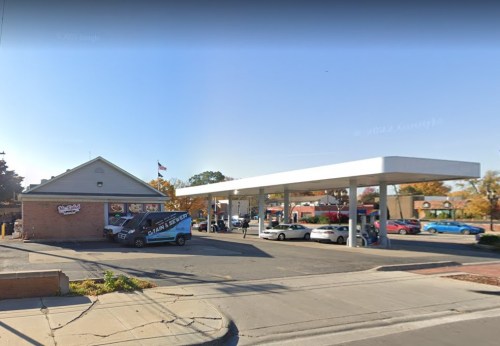 A gas station with a convenience store, cars parked, and a delivery van outside on a clear day.