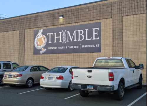 Sign for Thimble Brewery Tours & Taproom in Branford, CT, with parked cars in front of a brick building.