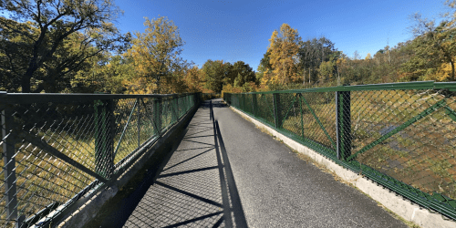 A pathway on a bridge surrounded by trees with autumn foliage under a clear blue sky.