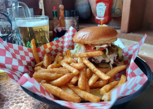 A burger with lettuce, tomato, and onions served with a side of golden fries and a glass of beer in the background.