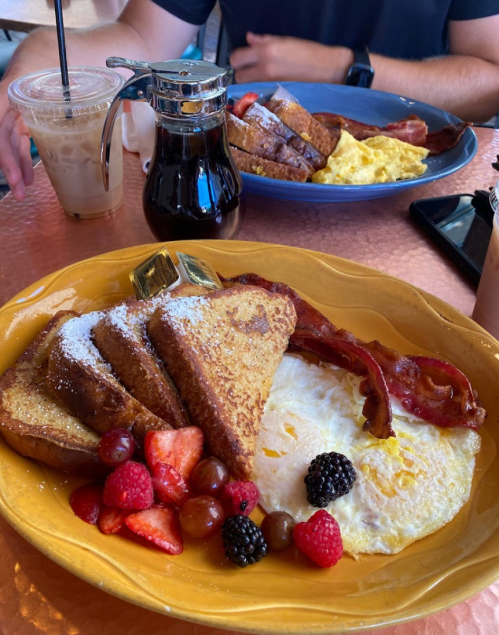 A plate of French toast with berries, bacon, and an omelet, alongside drinks on a table.