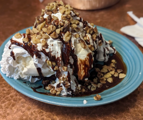 A dessert of whipped cream topped with chocolate sauce and chopped walnuts on a blue plate.