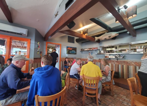 A cozy restaurant interior with wooden tables, patrons dining, and a fish-themed decor on the walls.
