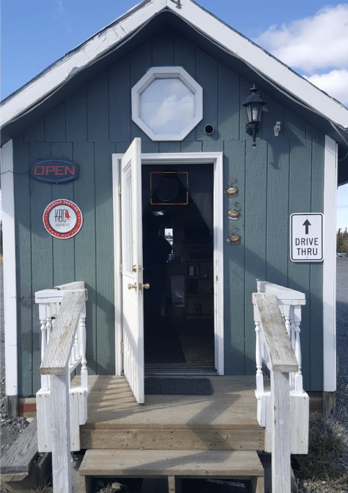 A small blue building with an open door, featuring a drive-thru sign and a welcoming atmosphere.