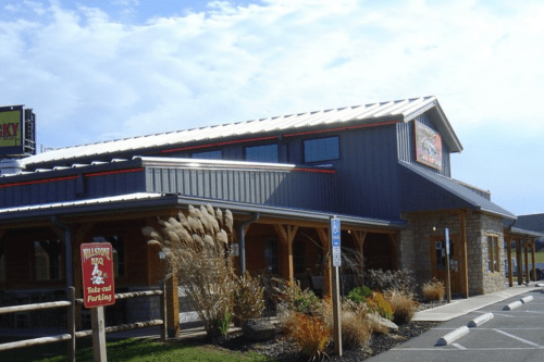 A rustic BBQ restaurant with a metal roof, wooden accents, and a sign indicating takeout parking.