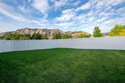 A spacious green lawn enclosed by a white fence, with mountains and a blue sky in the background.