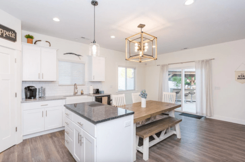 Bright, modern kitchen with white cabinets, a large wooden dining table, and sliding glass doors to an outdoor area.