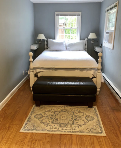 Cozy bedroom with a white bed, two lamps, a bench at the foot, and a decorative rug on wooden flooring.