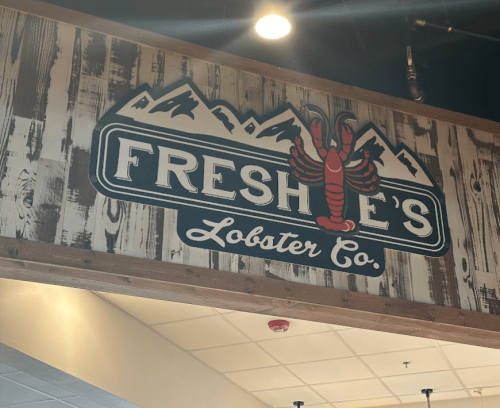Sign for Freshie's Lobster Co. featuring a lobster graphic and mountain design on a wooden background.