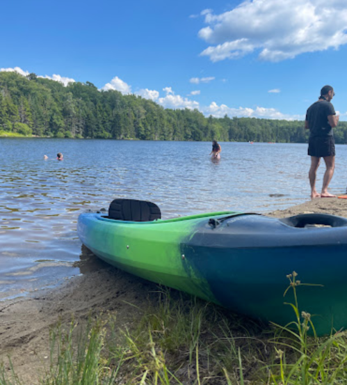 A kayak on the shore of a lake with people swimming and enjoying a sunny day in the background.