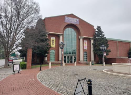 A brick building with large windows and banners, surrounded by trees and a cobblestone path.