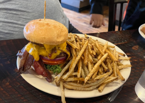 A juicy cheeseburger with bacon, lettuce, and tomato, served with a side of crispy fries on a white plate.